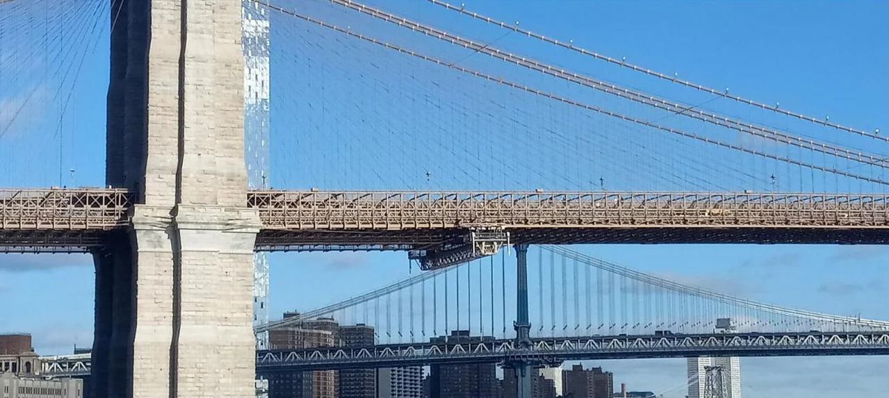 The stone tower and cables of the Brooklyn Bridge against a blue sky, with the Manhattan Bridge behind