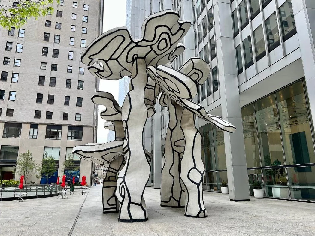 Black and white sculpted trees, taller than the people nearby, on a stone plaza