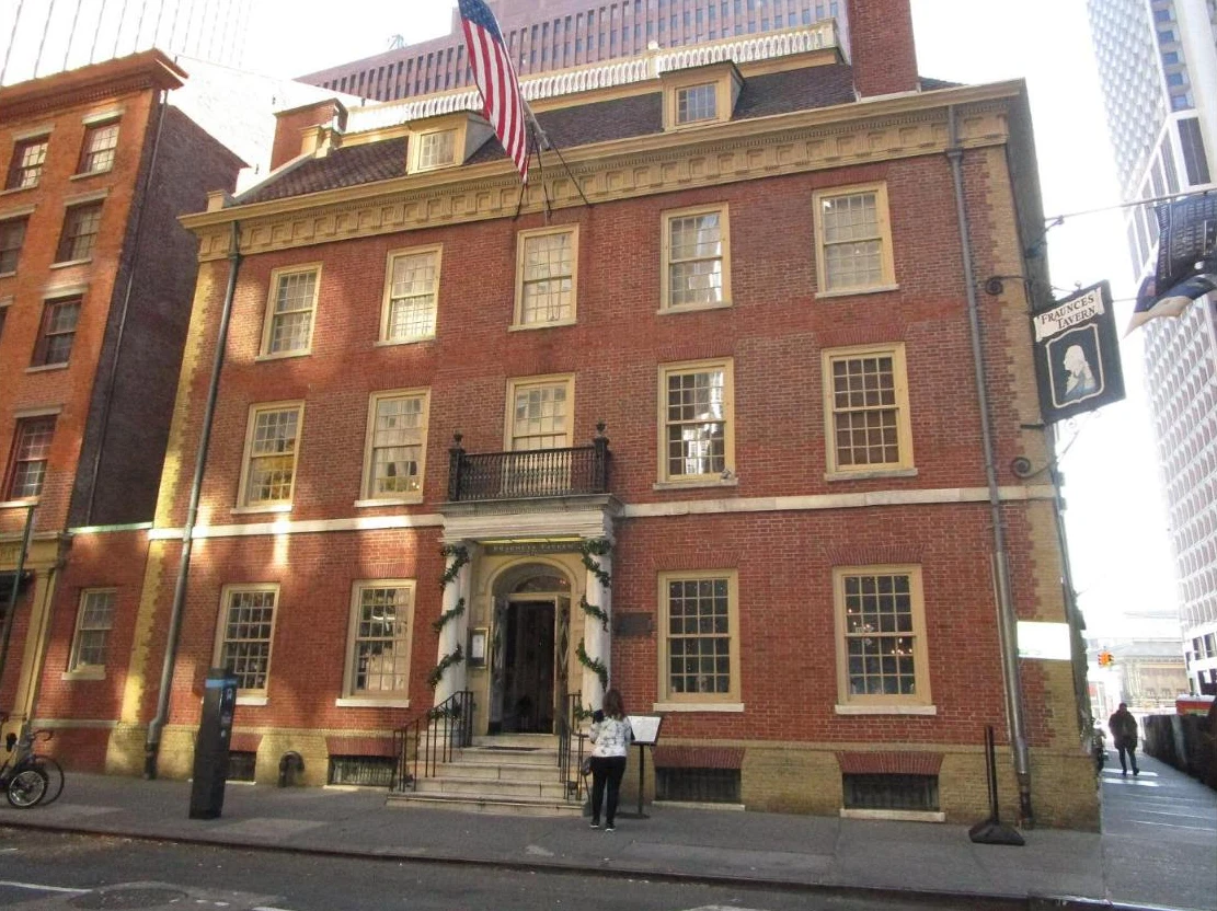 A red brick Georgian building with a hip roof, dormers and a hanging tavern sign