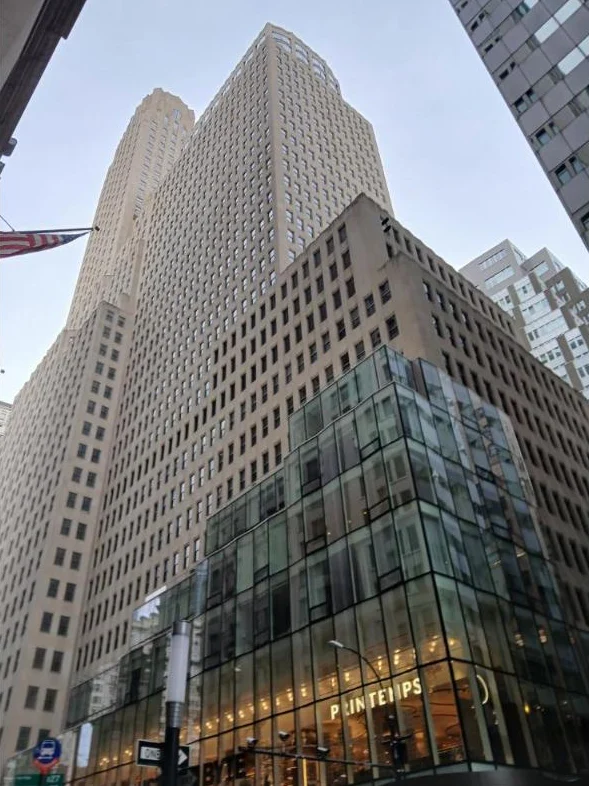 A tall pale limestone Art Deco tower with a glass-walled store at street level signed Printemps