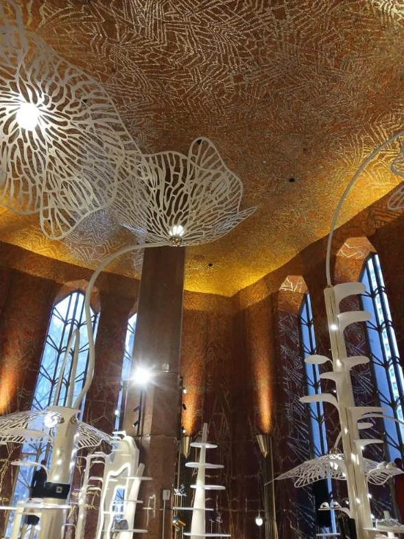 A soaring hall with glittering red, orange and gold mosaic walls and ceiling, tall arched windows and white sculptural displays