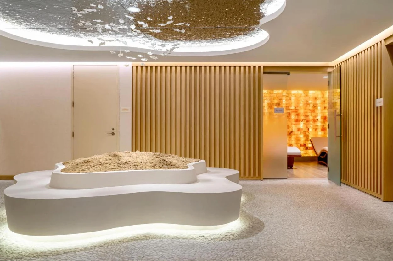 A sculptural spa lounge with a glowing pink salt-brick room through an open doorway