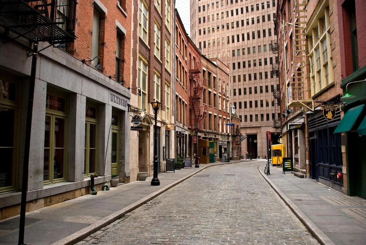 A narrow cobblestone lane lined with brick buildings, lamp posts and shop signs