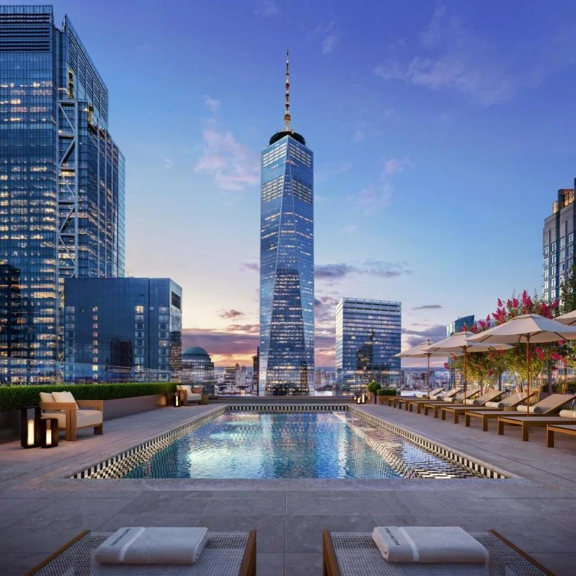 Rendering of a rooftop pool at dusk with lounge chairs and umbrellas, One World Trade Center glowing beyond
