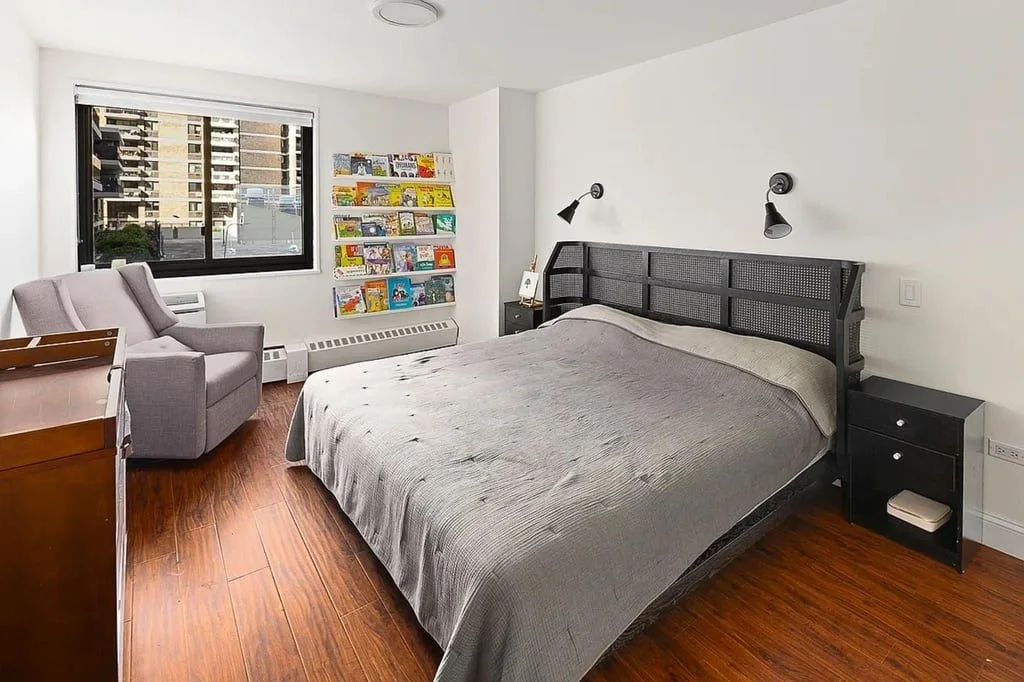 A bedroom with a grey upholstered bed, hardwood floors and a city view
