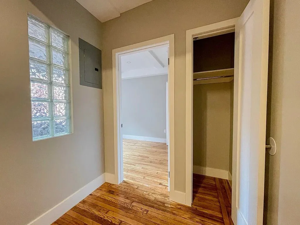 A hallway with a closet and doors to two rooms, with glass block windows