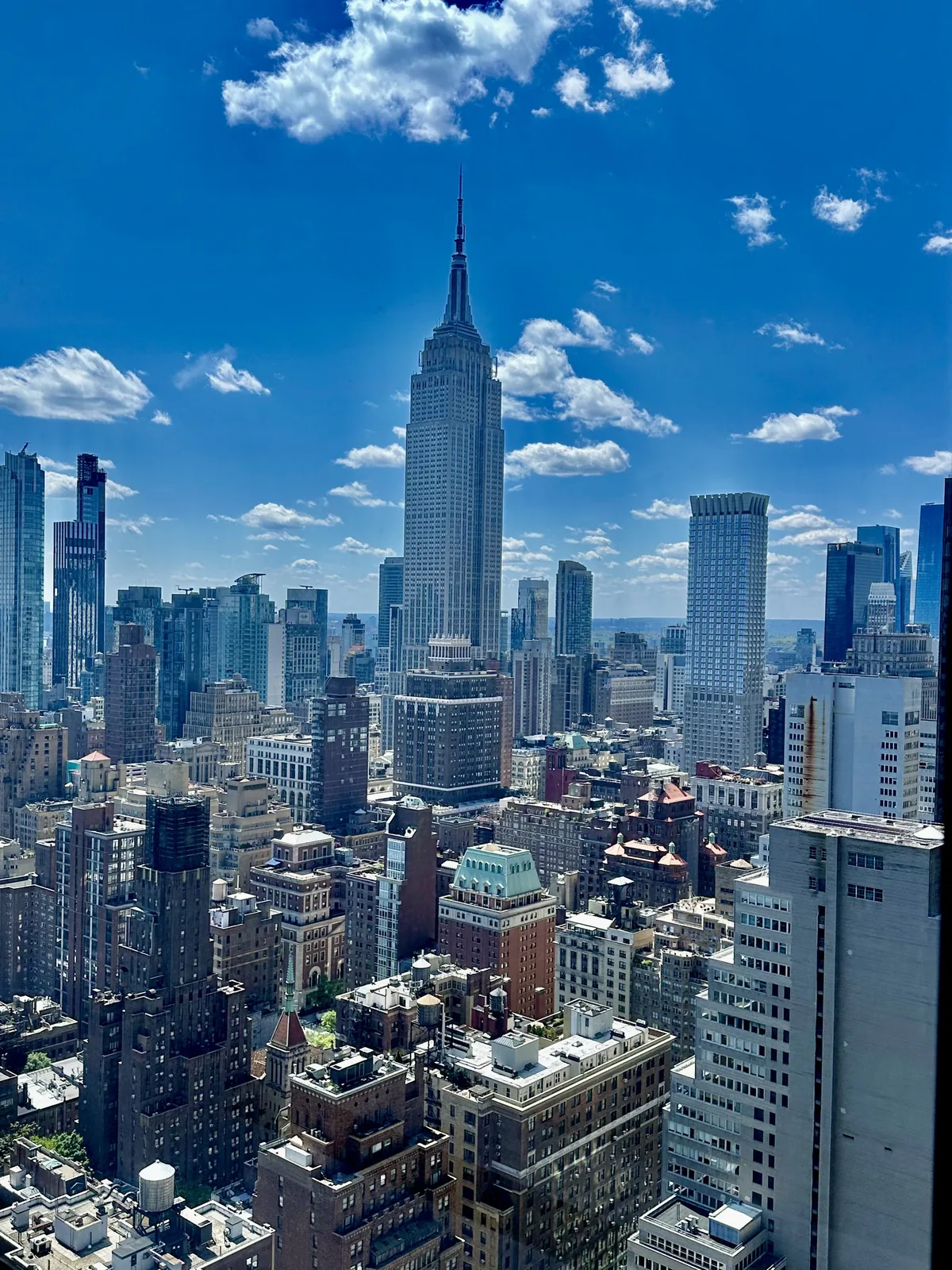 The Empire State Building rising above Midtown Manhattan under a bright blue sky, seen from a high-floor apartment in Kips Bay